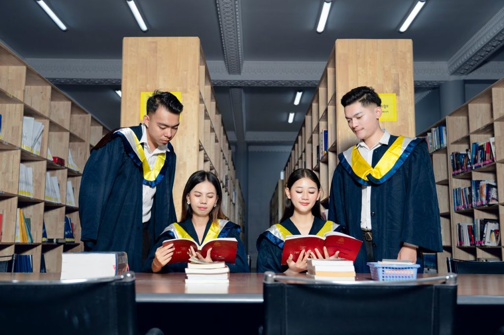 A group of university graduates in academic gowns study together in a library.
