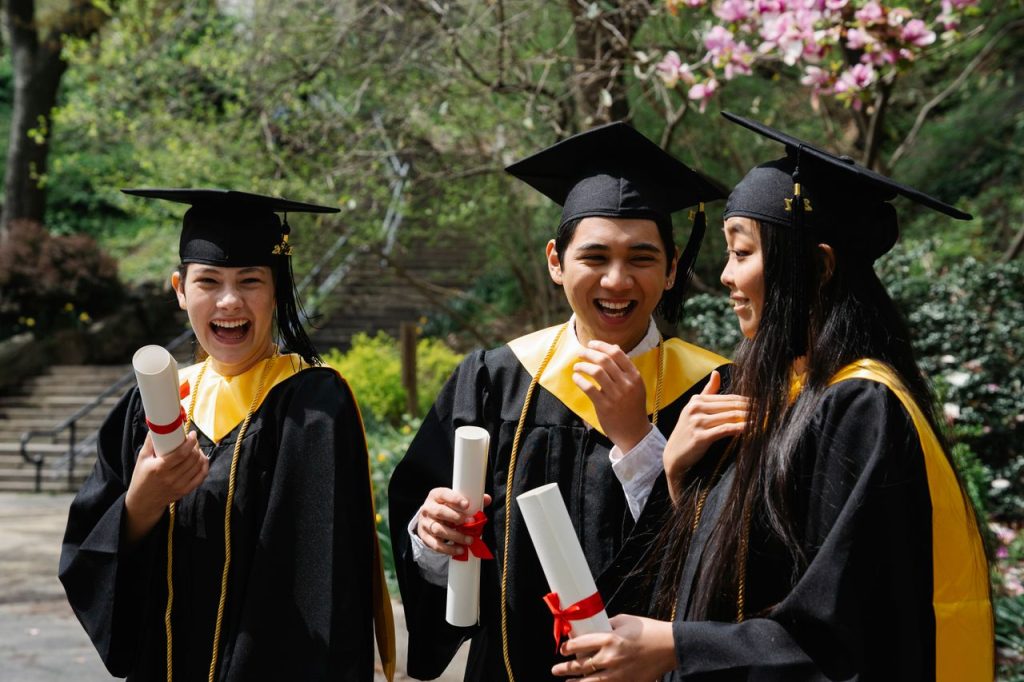Group of diverse students celebrating graduation with diplomas outdoors.
