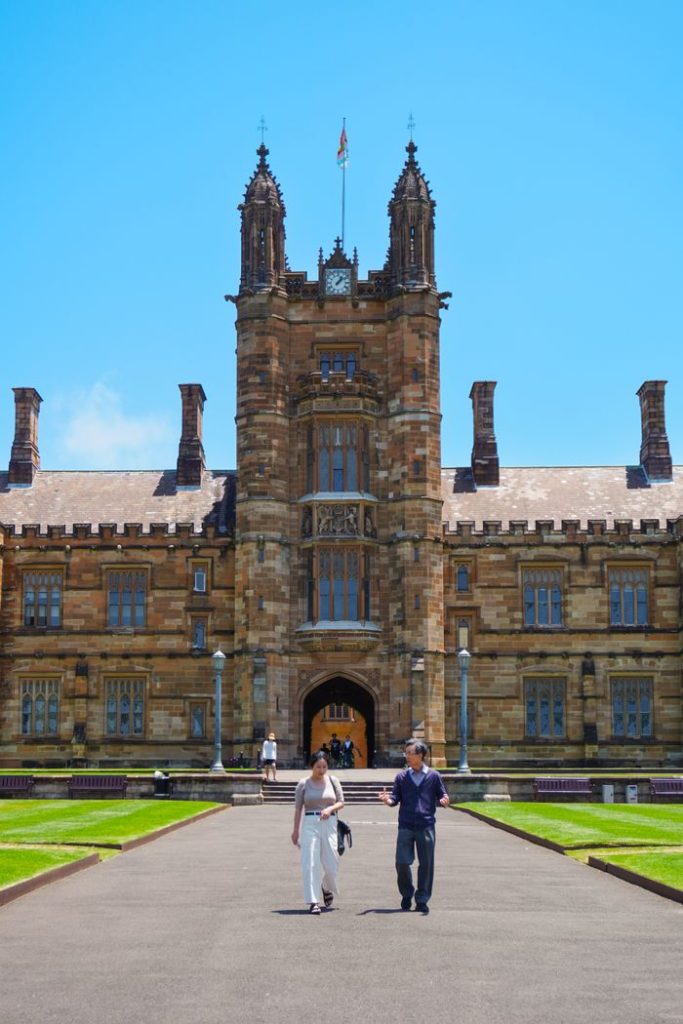 Historic university building facade with people walking on a sunny day.